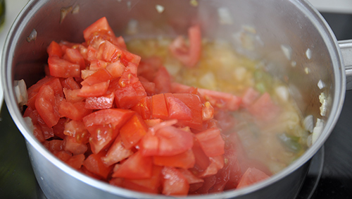 Echando el tomate cortado para hacer salsa de tomate para pasta